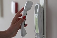 Eine Hand hält einen Telefonhörer neben einer Wand-Telefonstation.