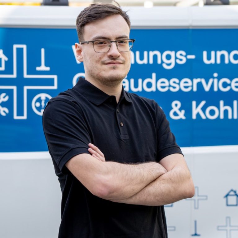 Mann mit verschränkten Armen vor einem Fahrzeug mit Dienstleistungsbeschriftung.