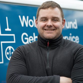 Lächelnder junger Mann mit verschränkten Armen vor einem weißen Lieferfahrzeug.