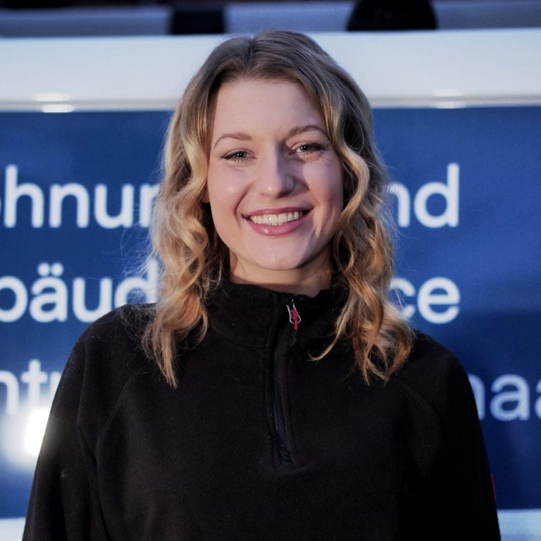 Junger Mann mit verschränkten Armen vor einem Firmenfahrzeug der Firma Henko.