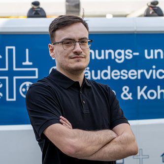 Mann mit verschränkten Armen vor einem Fahrzeug mit Dienstleistungsbeschriftung.