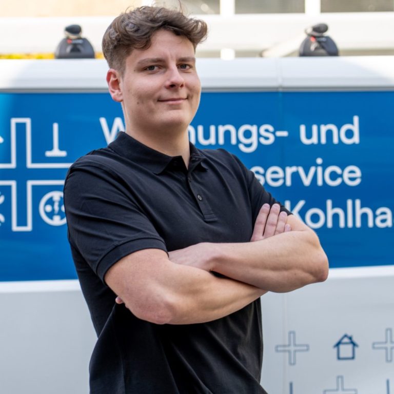 Mann mit verschränkten Armen vor einem Fahrzeug mit Dienstleistungsbeschriftung.