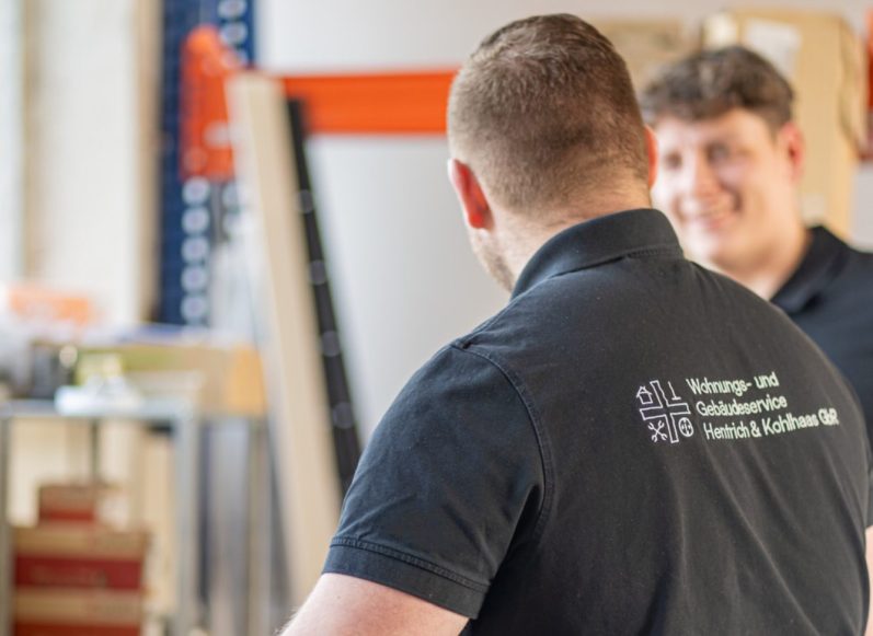 Zwei Personen in Arbeitskleidung, eine schaut zur anderen und lächelt.