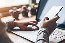 Eine Person nutzt ein Smartphone, während sie an einem Laptop arbeitet.
