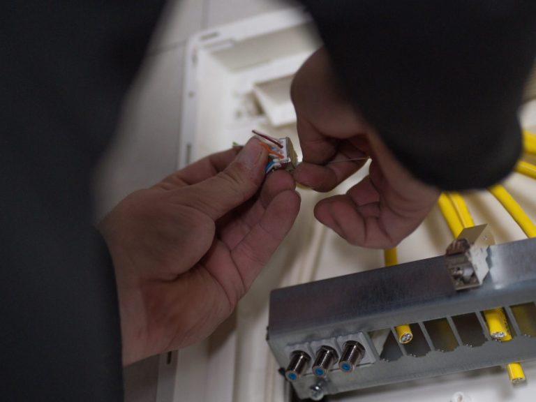 Hände schließen einen Stecker an eine Metallplatte mit mehreren Anschlüssen an.