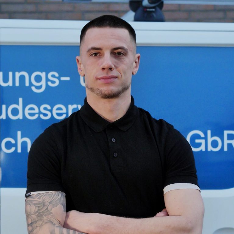 Junger Mann mit verschränkten Armen vor einem Firmenfahrzeug der Firma Henko.