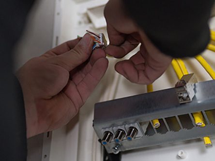 Hände schließen einen Stecker an eine Metallplatte mit mehreren Anschlüssen an.