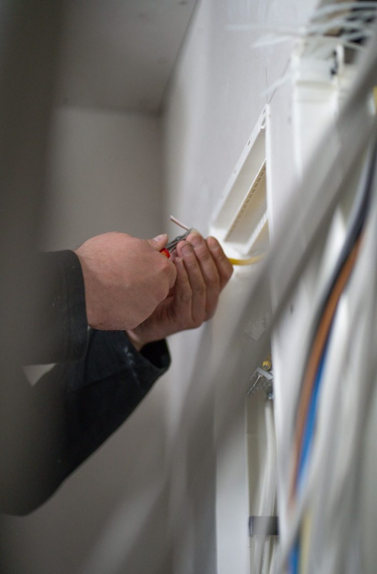 Händed mit einem Werkzeug, die Kabelinstallation an einer Wand vorbereitend.