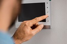 Hand drückt einen Knopf an einem Wandthermostat.