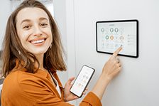 Lächelnde Frau benutzt ein Tablet und ein Smartphone zur Steuerung eines Geräts.
